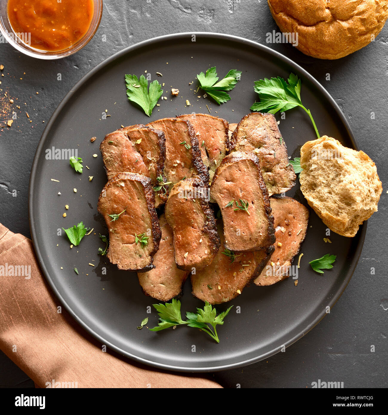 Close up of grilled sliced beef liver on plate over black stone