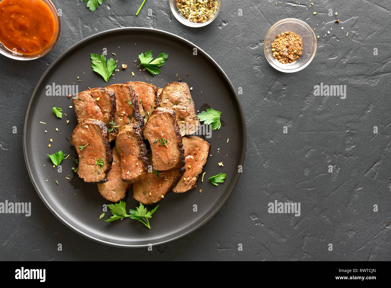 Grilled sliced beef liver on plate over black stone background. Cooked