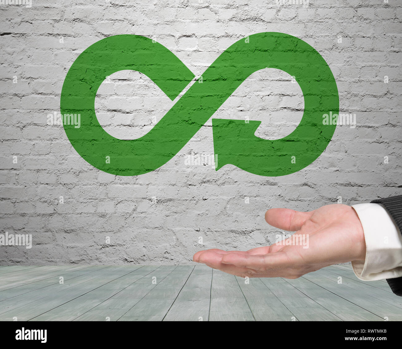 Green circular economy concept. Hand showing arrow infinity symbol on brick wall. Stock Photo