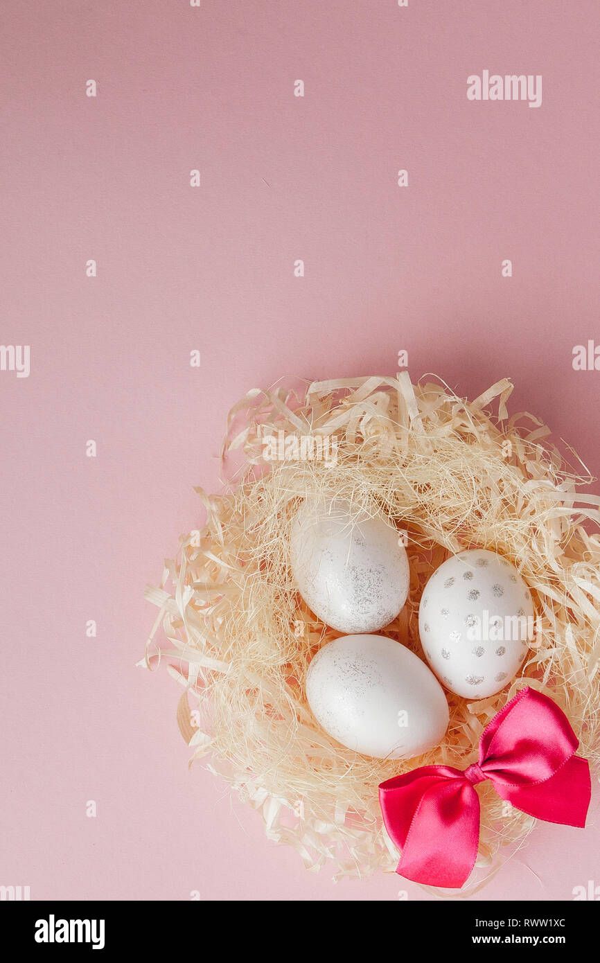 White Easter eggs in a nest on pink background. Design pastel tone in ...