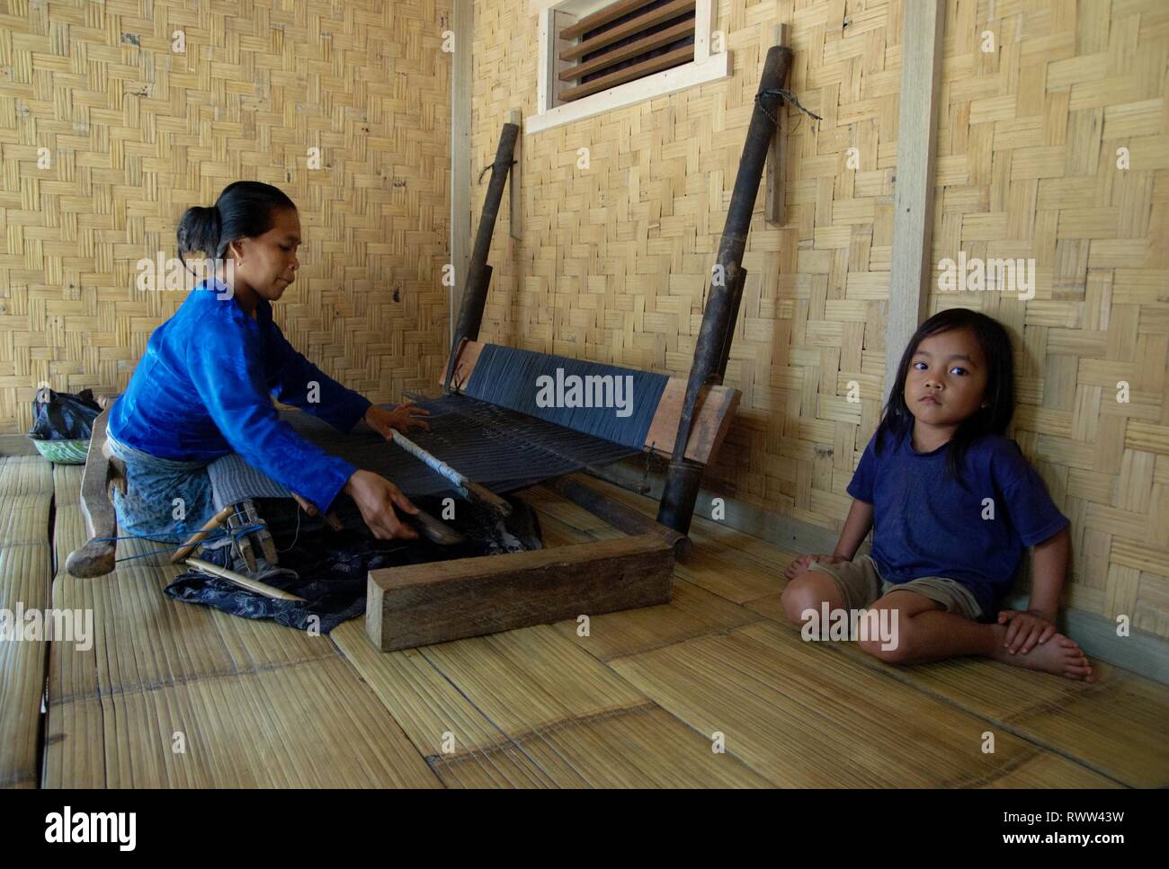 A mother works with her traditional weaving machine, while her daughter are sitting next to her. Location : Baduy, Banten, Indonesia. Stock Photo