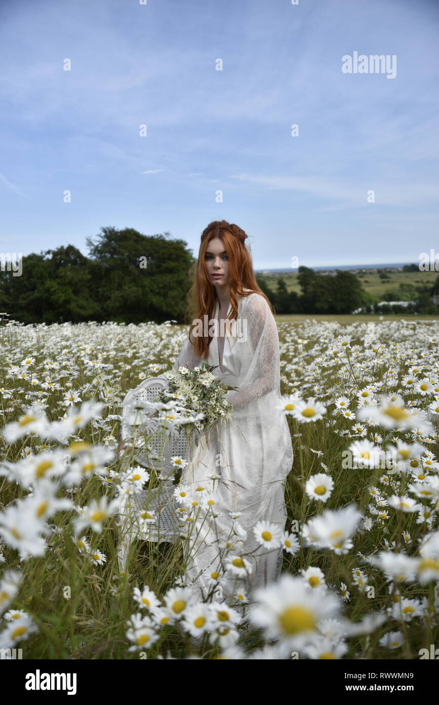 A beautiful red haired girl in a long white dress poses in the middle ...