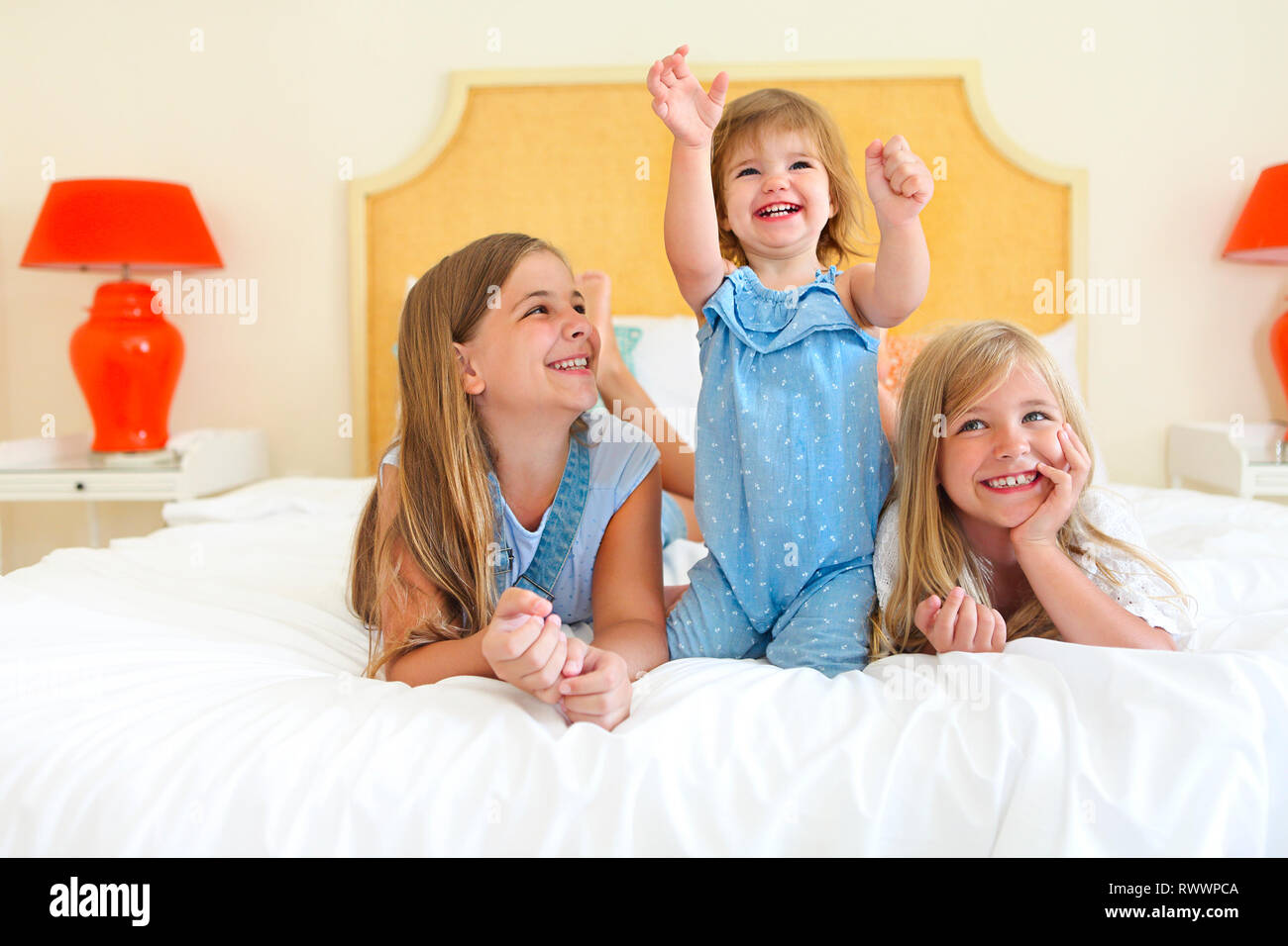 Three happy little sisters on a bed having fun Stock Photo