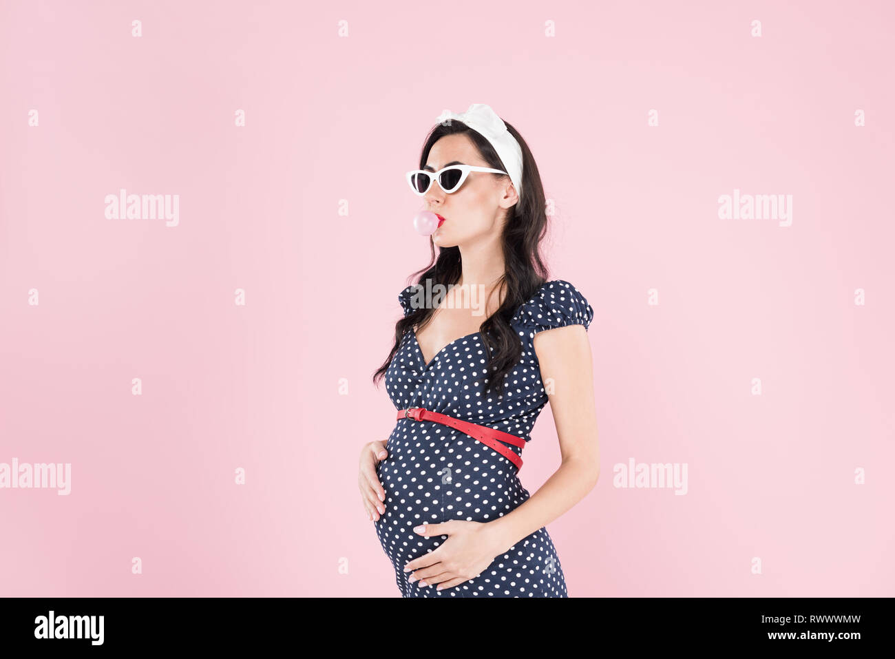 Pregnant woman in sunglasses chewing bubble gum isolated on pink Stock