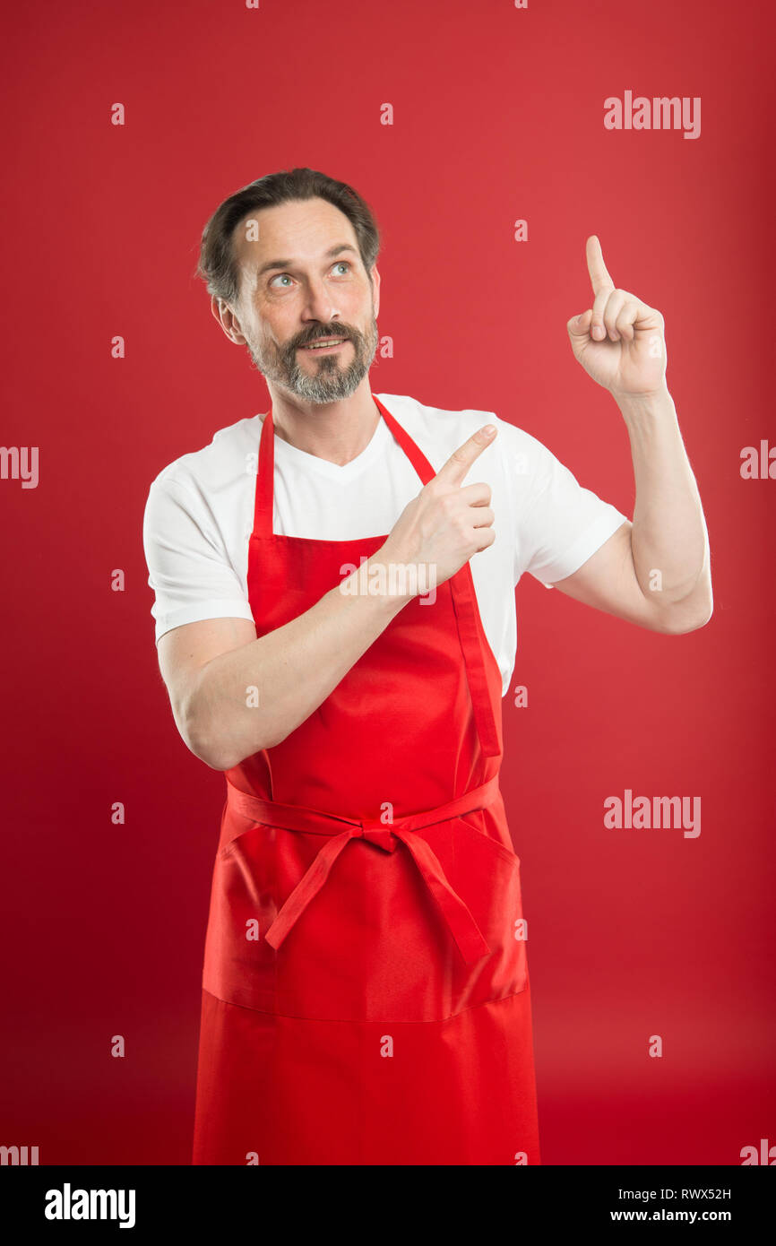 Inventing new dish. Cook with beard and mustache wear apron red background. Man mature cook posing cooking apron. Chief cook and professional culinary. Cook food at home. Fine recipe. Ideas and tips. Stock Photo