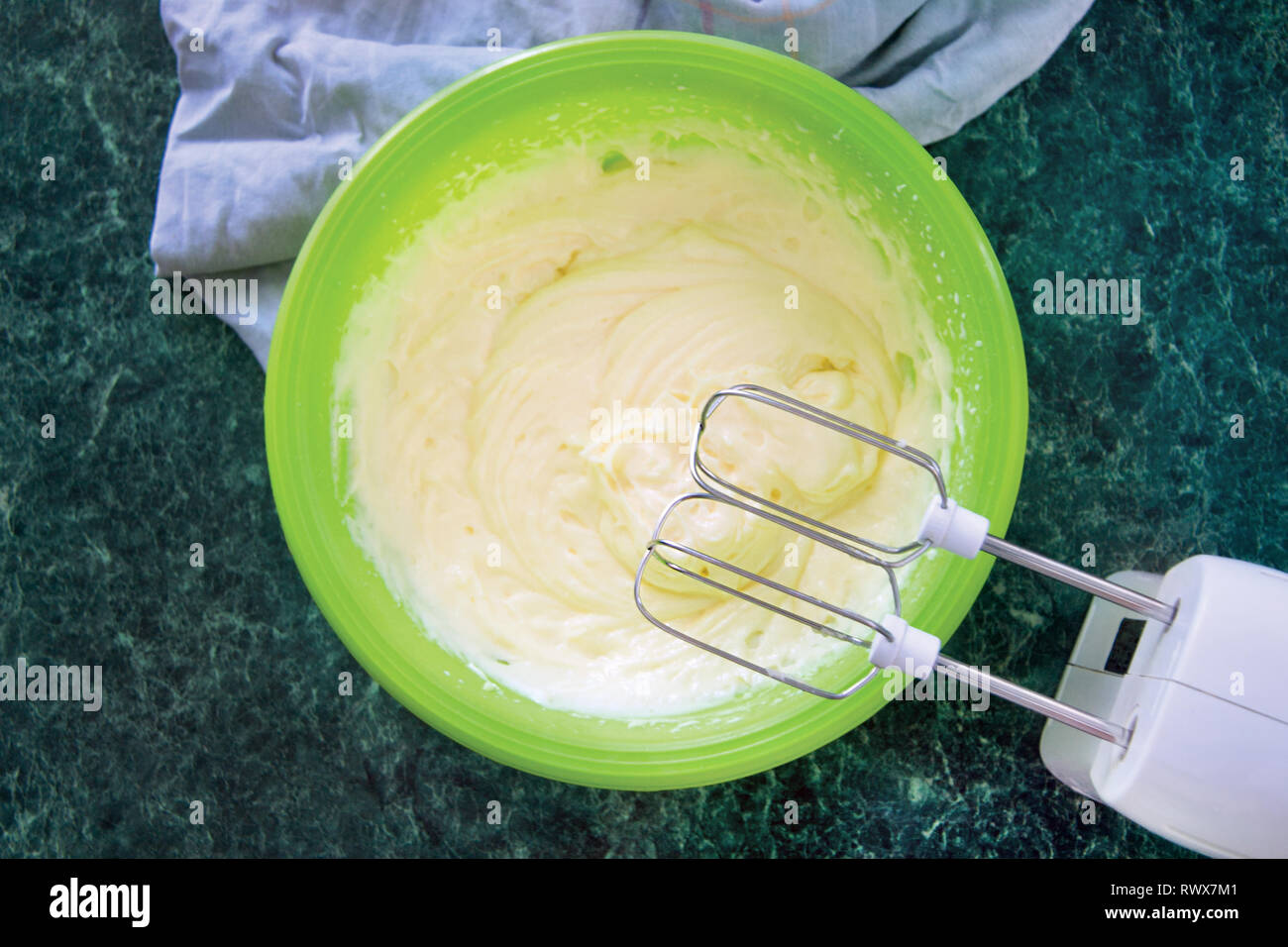 The process of cooking napoleon cake, mixer in bowl whips sweet cream on a green marble table, top view. Recipe dessert. Stock Photo