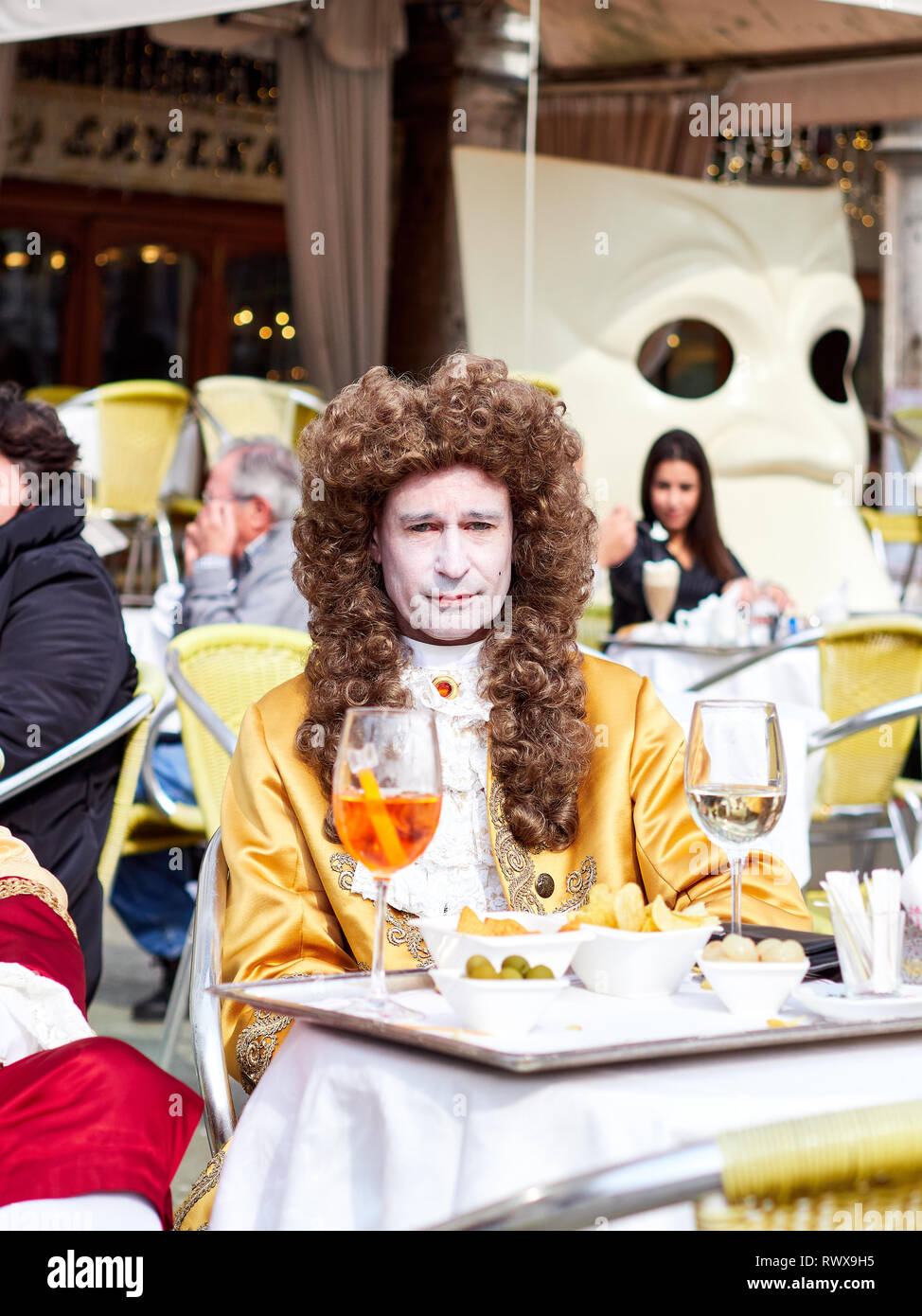 Venice, Italy - March 1, 2019 Men dressed with a wig and a costume having a drink in Piazza San Marco during Carnival of Venice Stock Photo
