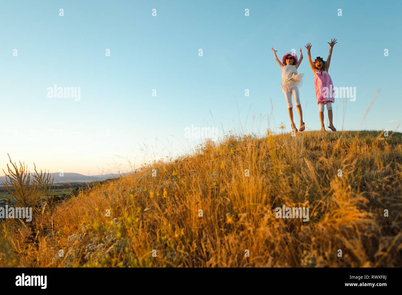 Two joyful children jumped and raised hands up. Captured emotion during sunset after summer day. Stock Photo