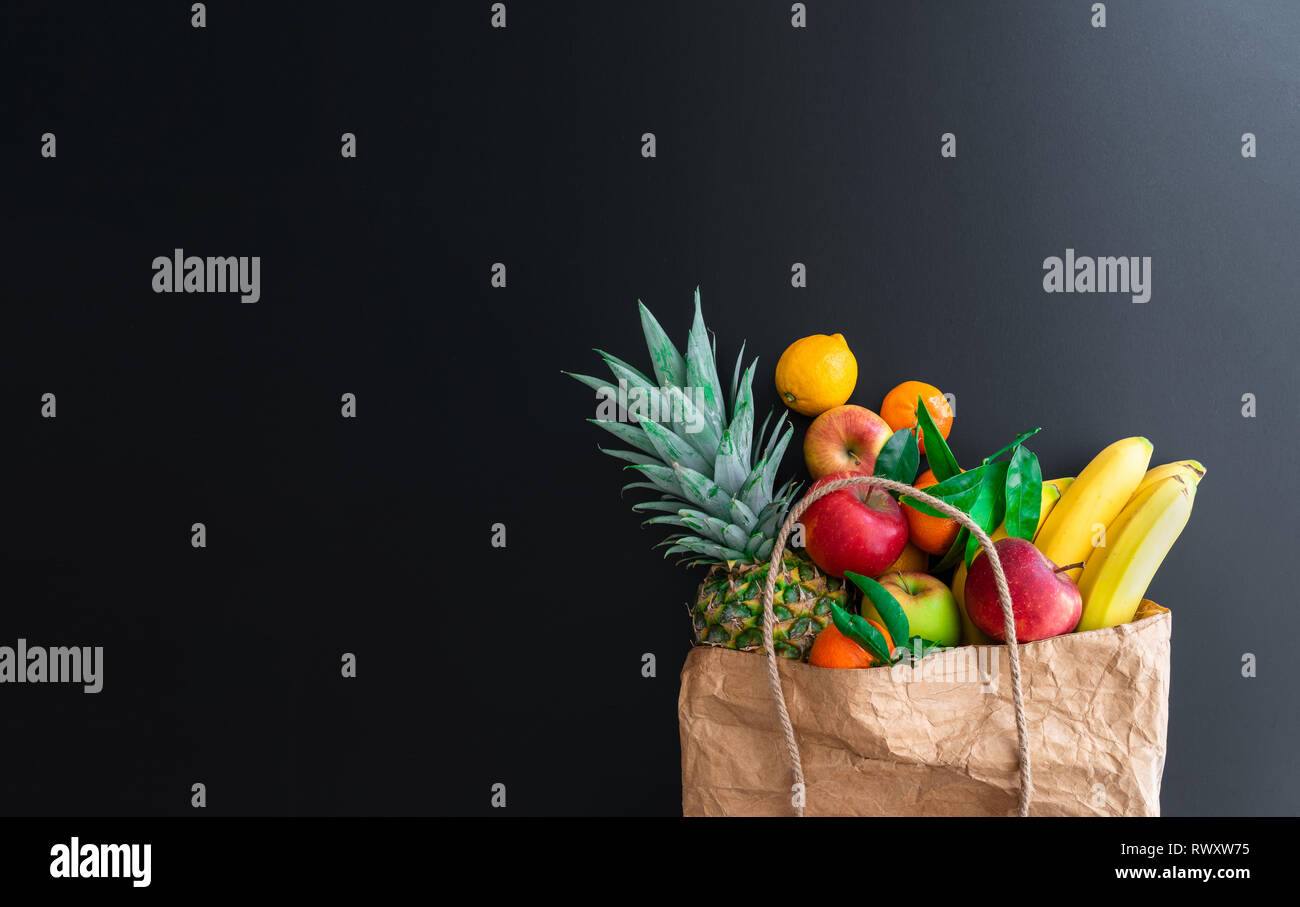 fresh healthy organic fruits bought on weekly market in brown paper bag against dark table background Stock Photo