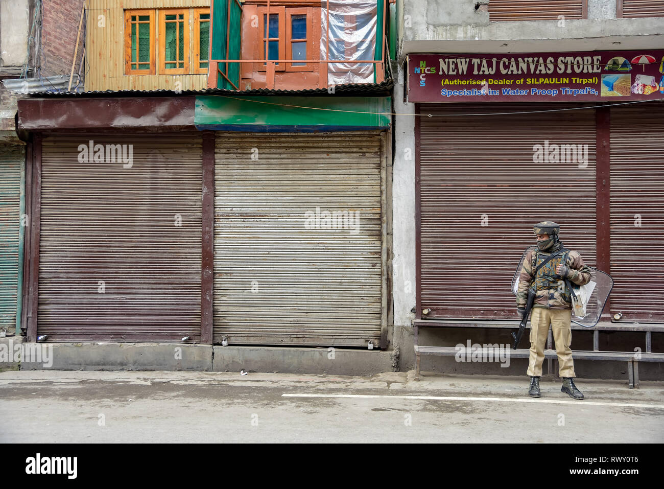 A paramilitary man seen standing on guard in-front of closed shops during the shut-down in Srinagar. A shut-down is being observed in Maisuma area of Srinagar city. Jammu and Kashmir Liberation Front chairman Yasin Malik who was detained on February 22 was booked under Public Safety Act (PSA) and shifted to Kot Balwal jail in Jammu earlier today. Stock Photo
