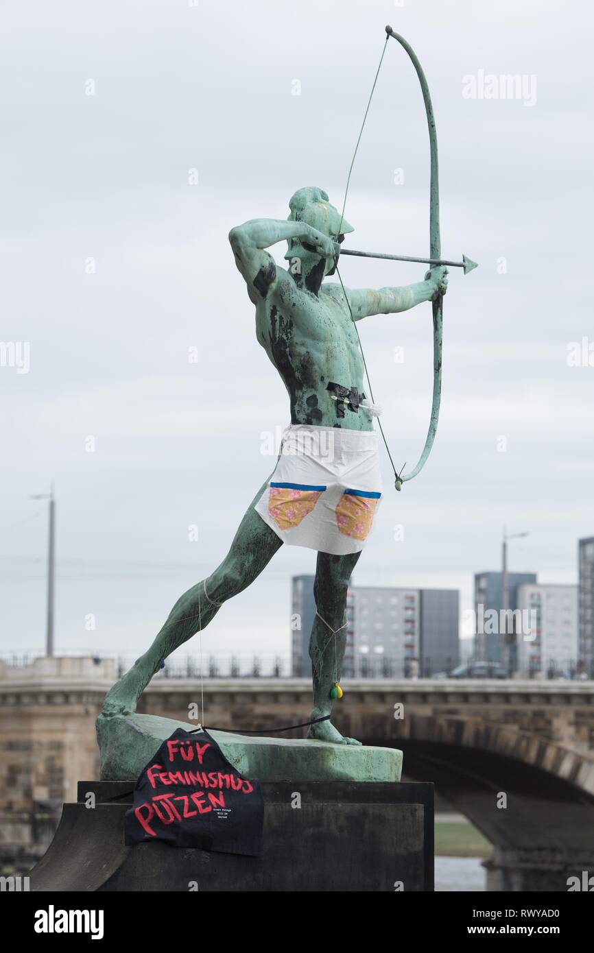 Dresden, Germany. 08th Mar, 2019. A toilet brush as well as an apron and a black fabric with the inscription 'Für Feminismus Putzen' hang on the sculpture 'Archer' by Ernst Moritz Geyger. The action falls on the International Women's Day, which is celebrated on the same day. Credit: Sebastian Kahnert/dpa-Zentralbild/dpa/Alamy Live News Stock Photo