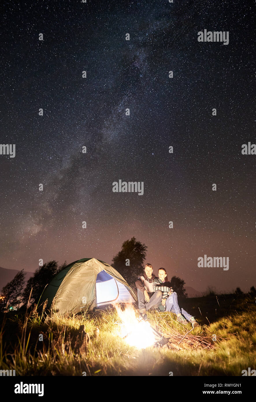 Young happy couple hikers resting at campfire near tourist tent in the ...