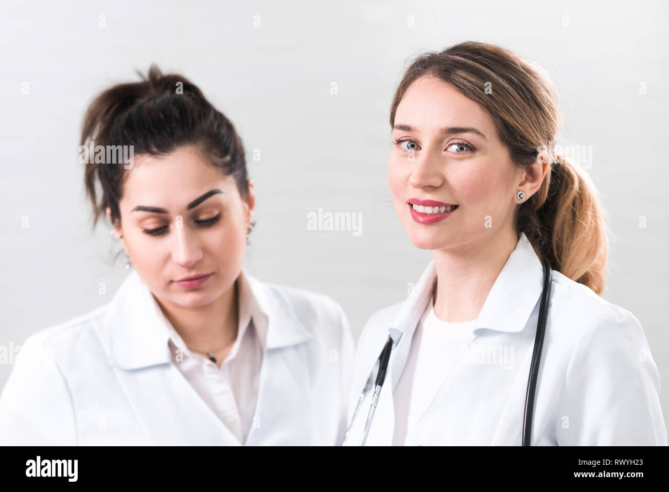 Two female assistants dressed in white coats talking to each other in