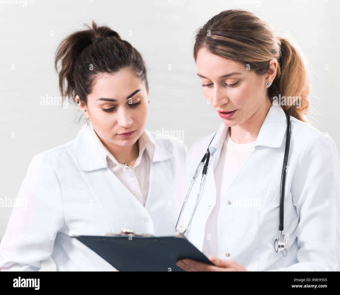 Two female assistants dressed in white coats talking to each other in