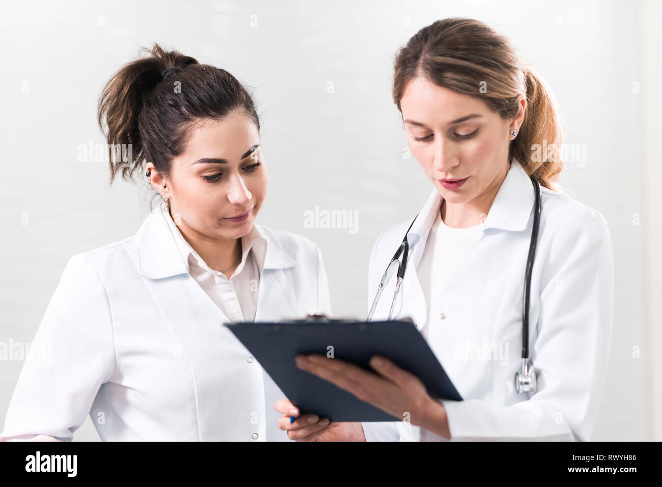 Two female assistants dressed in white coats talking to each other in