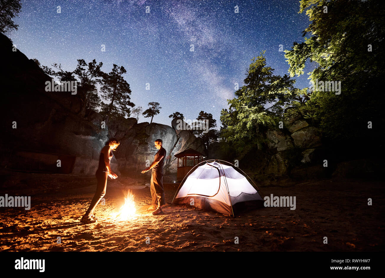 Young couple tourists man and woman resting beside camp and illuminated ...