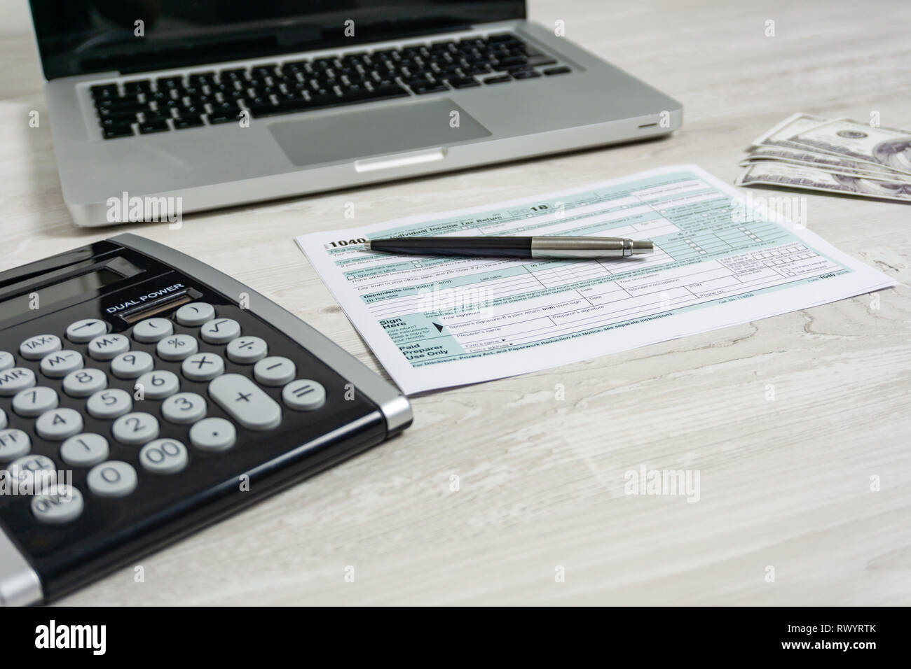 US tax form next to computer laptop, dollar bills, calculator and tax form 1040. tax form us business income office hand fill concept Stock Photo