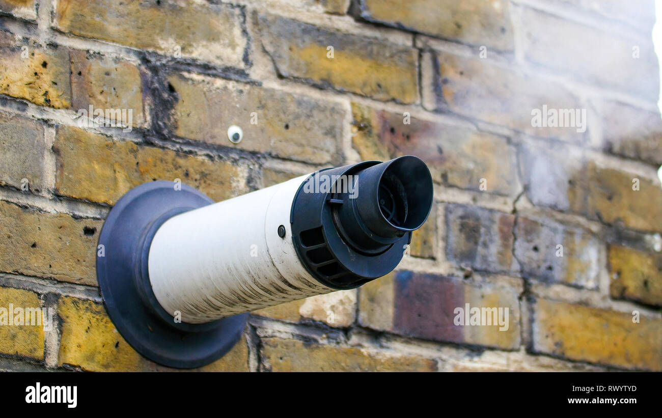 A steam coming out from a ventilation in a wall. The white smoke coming out from the steam may comes from the building inside Stock Photo