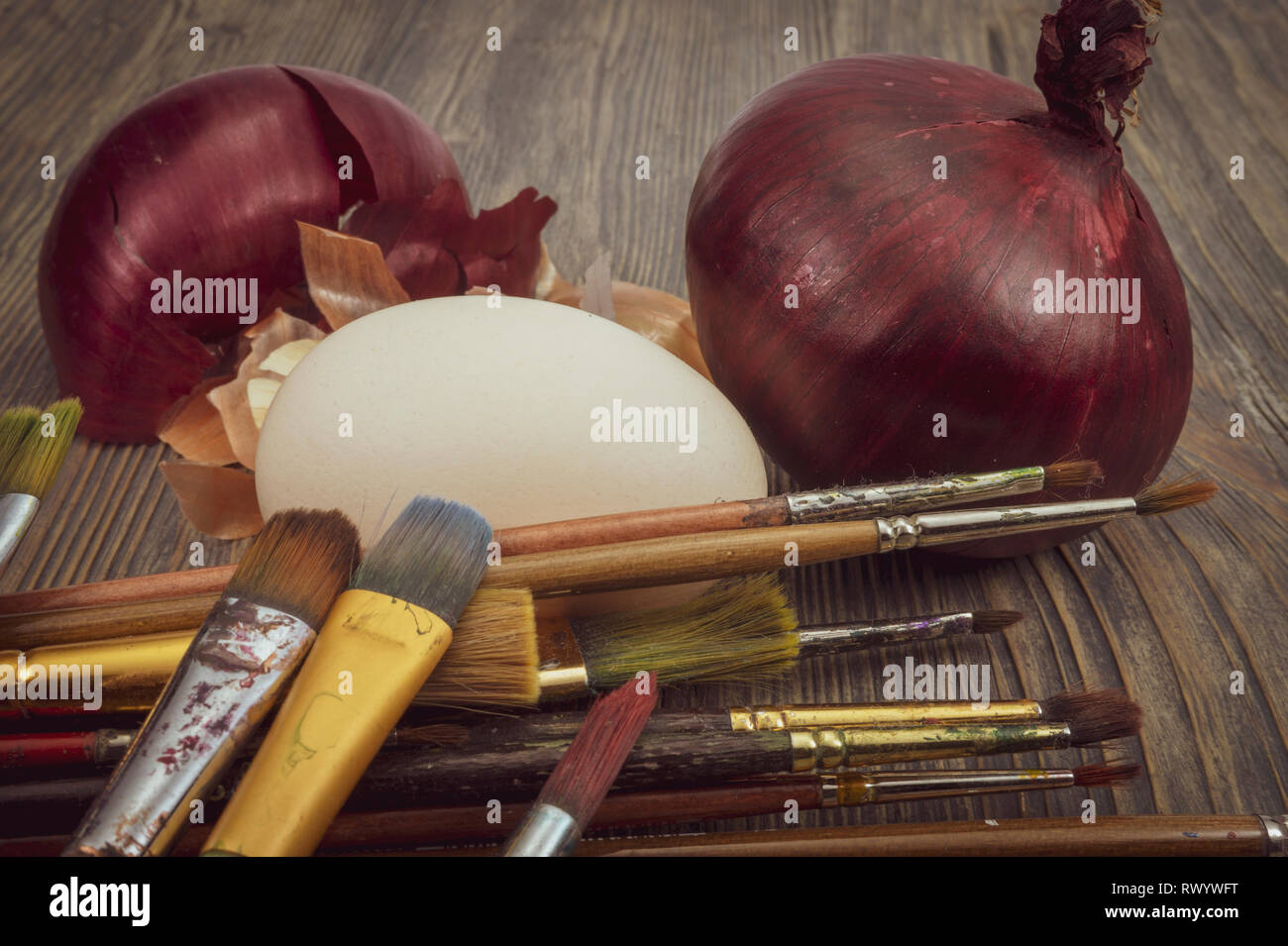 Fresh egg, painting brushes, whole red onion and dried onion skin on a