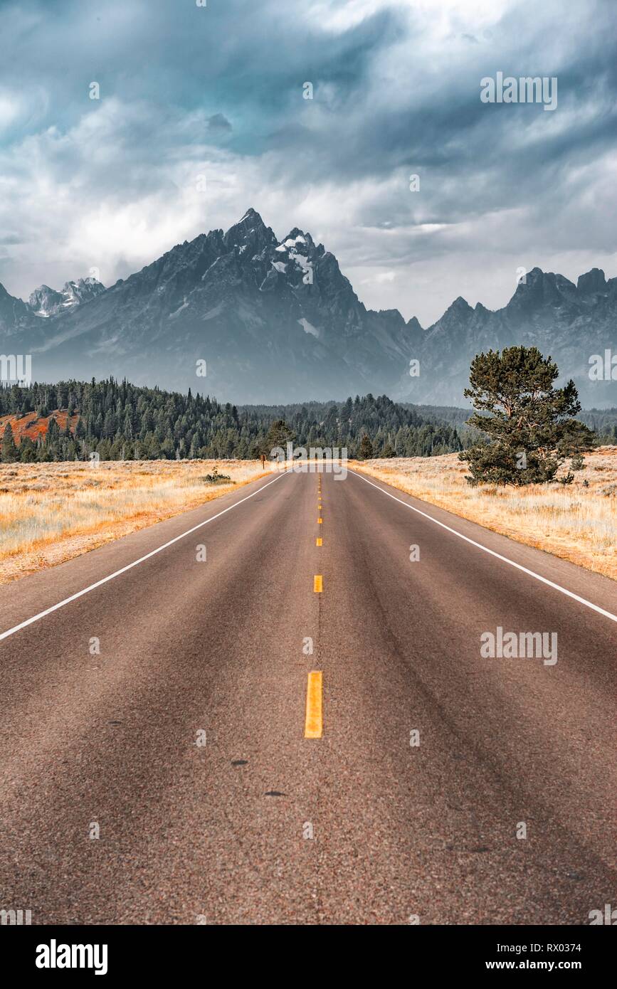 Highway in front of rugged mountains with cloudy skies, Grand Teton Range, Grand Teton National Park, Wyoming, USA Stock Photo