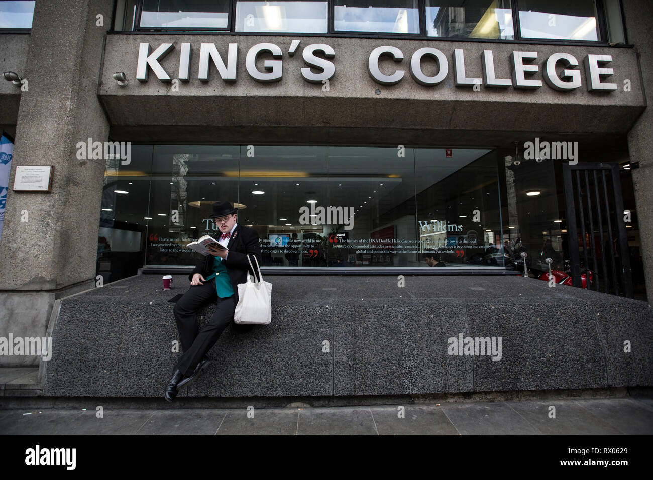 A smartly dressed student sitting on a wall of the facade of King's College Strand Campus, King's College London, England, UK Stock Photo