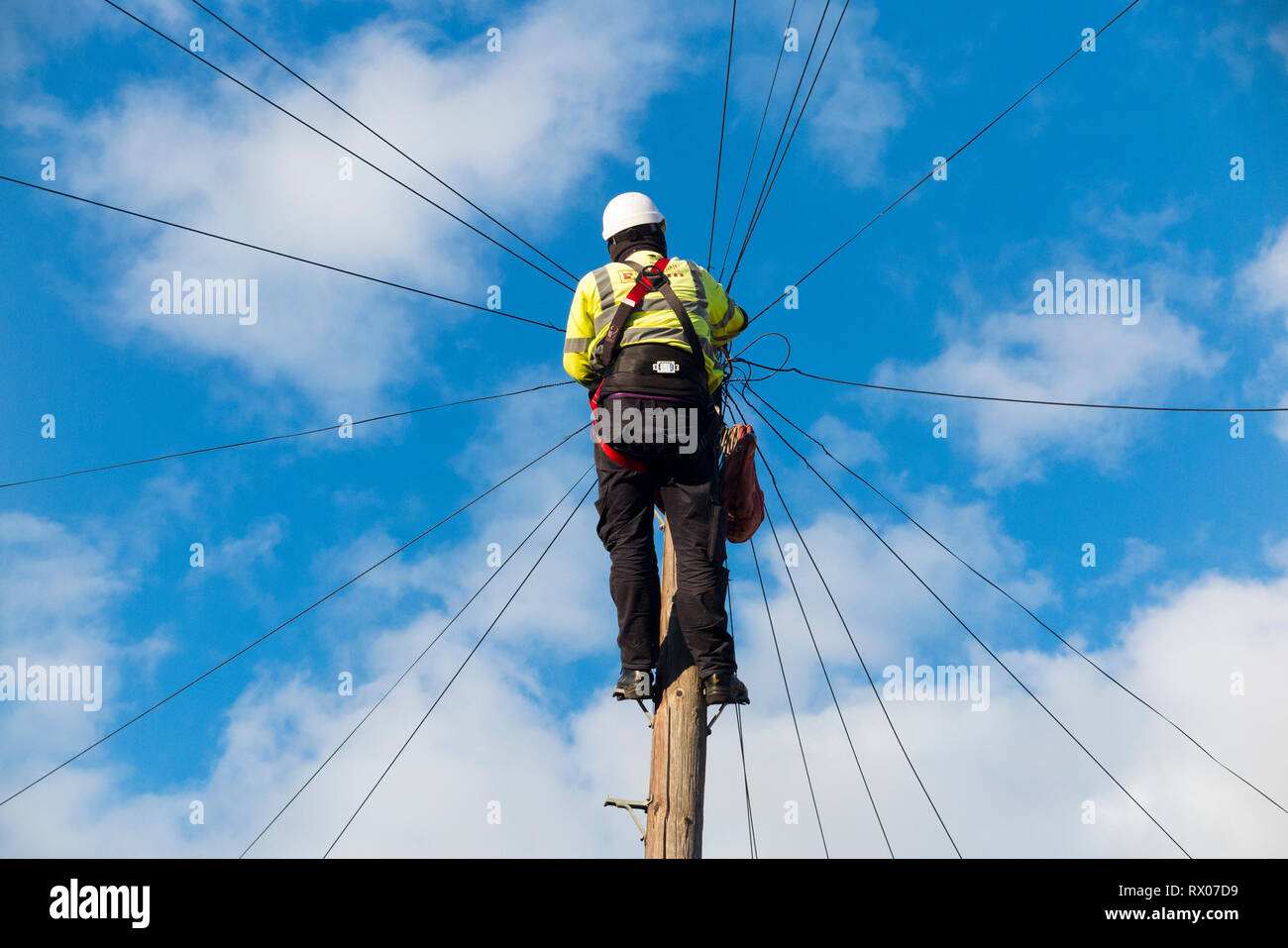 Telecom engineer working on domestic phone line / broadband internet copper wire up a telephone / telegraph pole in a London Street / Road, & blue sky Stock Photo