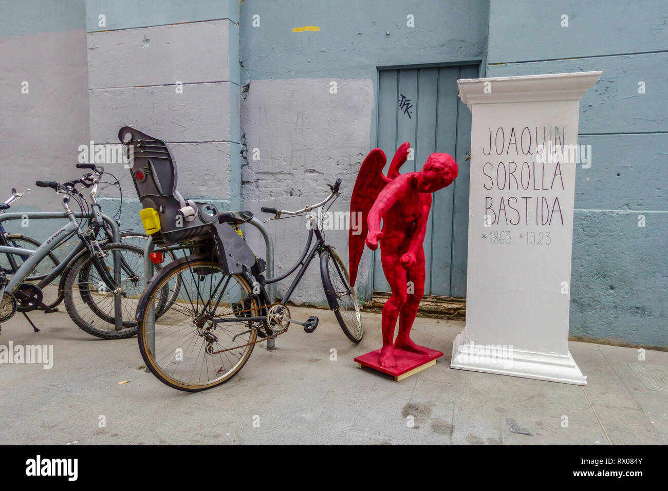 A red angel standing next to a bicycle in the street, Preparation for the festival Las Fallas, Valencia, Old Town, El Carmen district Stock Photo