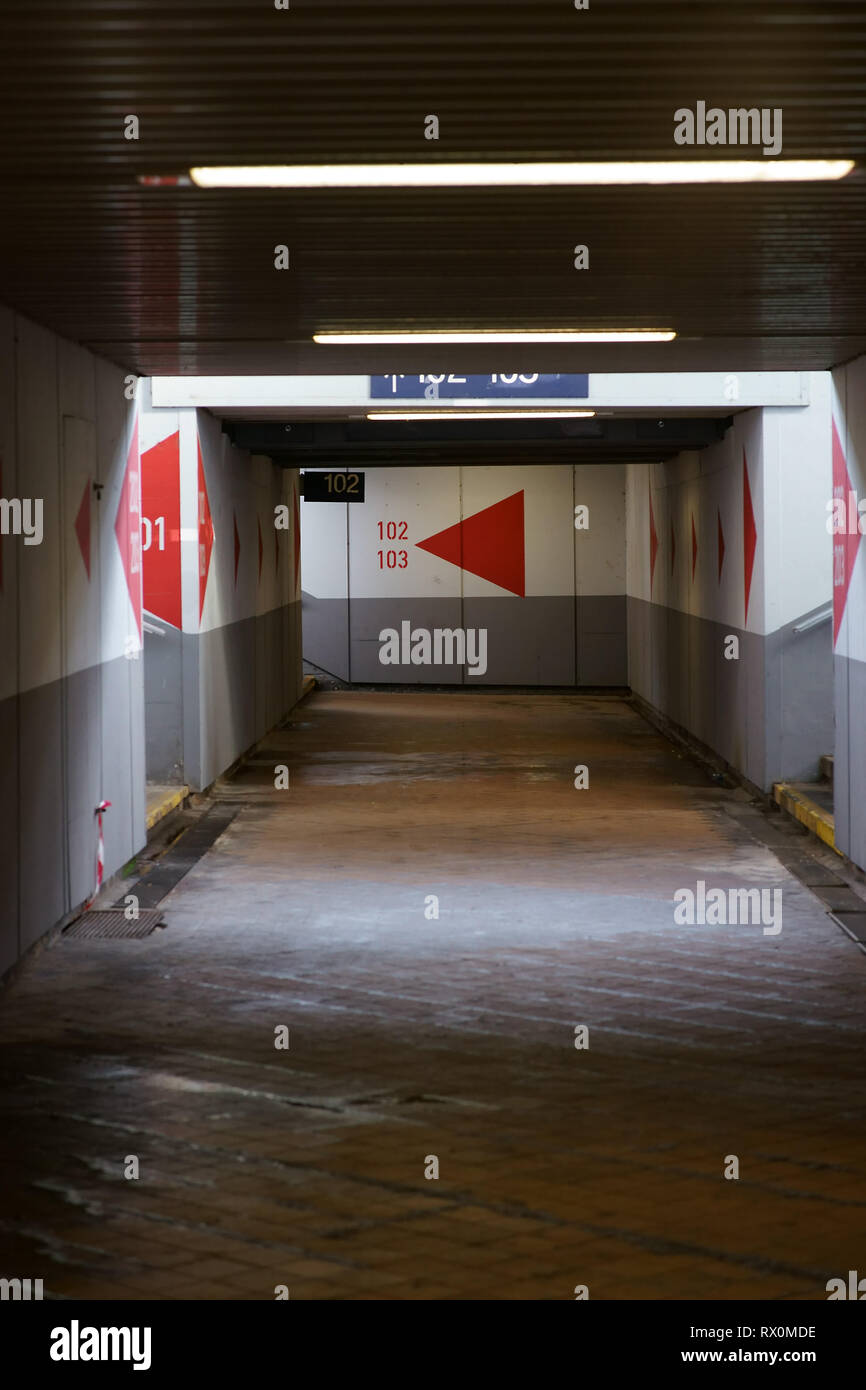 The deep corridor of a station tunnel with painted directional arrows, deck lighting and concrete walls. Stock Photo