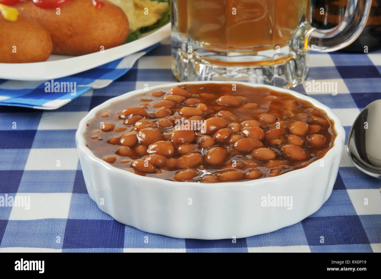 A bowl of baked beans on a picnic table with beer and corn dogs Stock