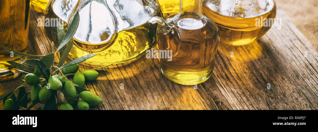 Olive oil in glass bottles and a green fresh olives twig on wooden table, banner, closeup view Stock Photo