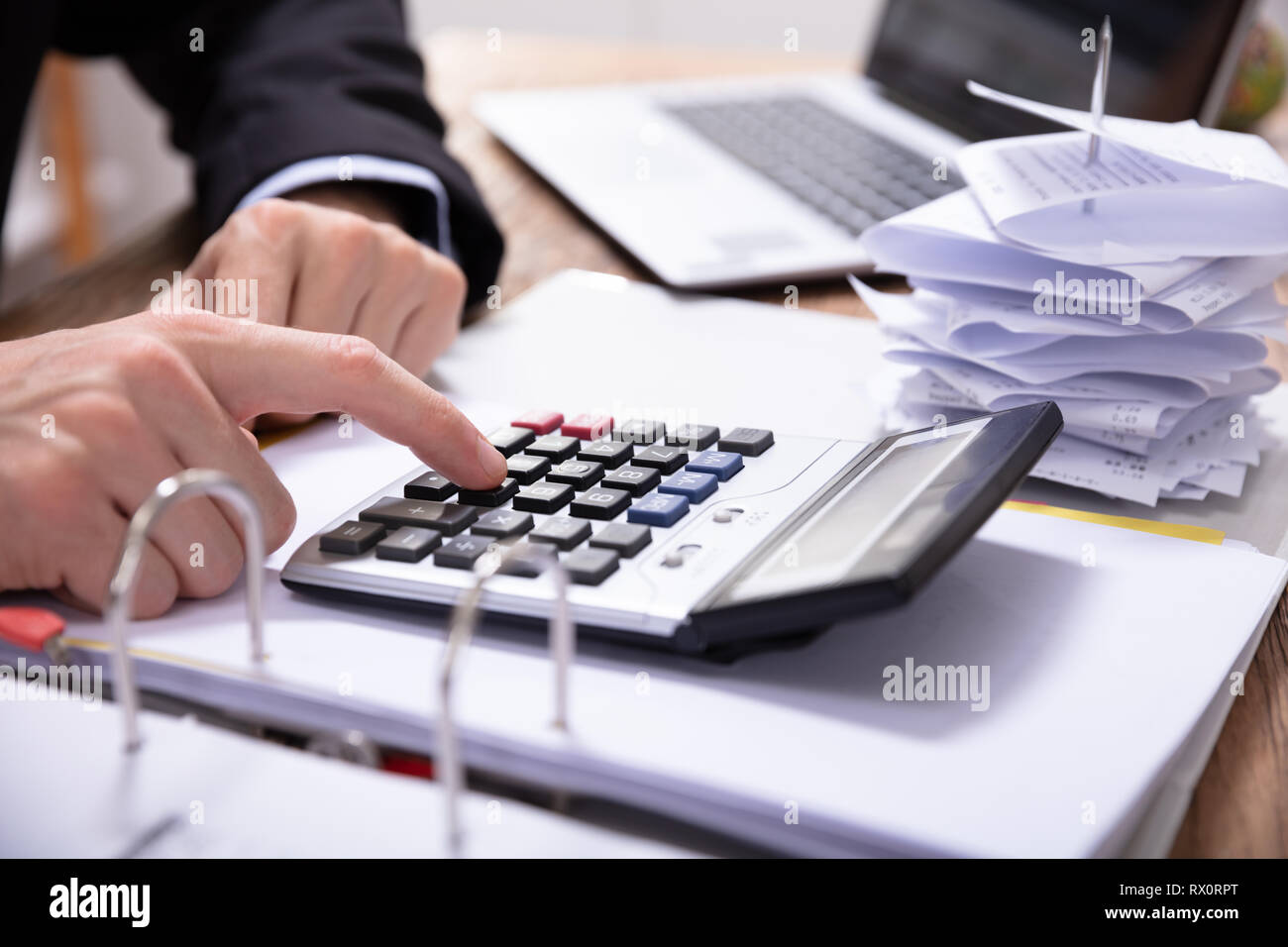 Close-up Of Businessman's Hand Using Calculator While Calculating Invoice On Desk Stock Photo