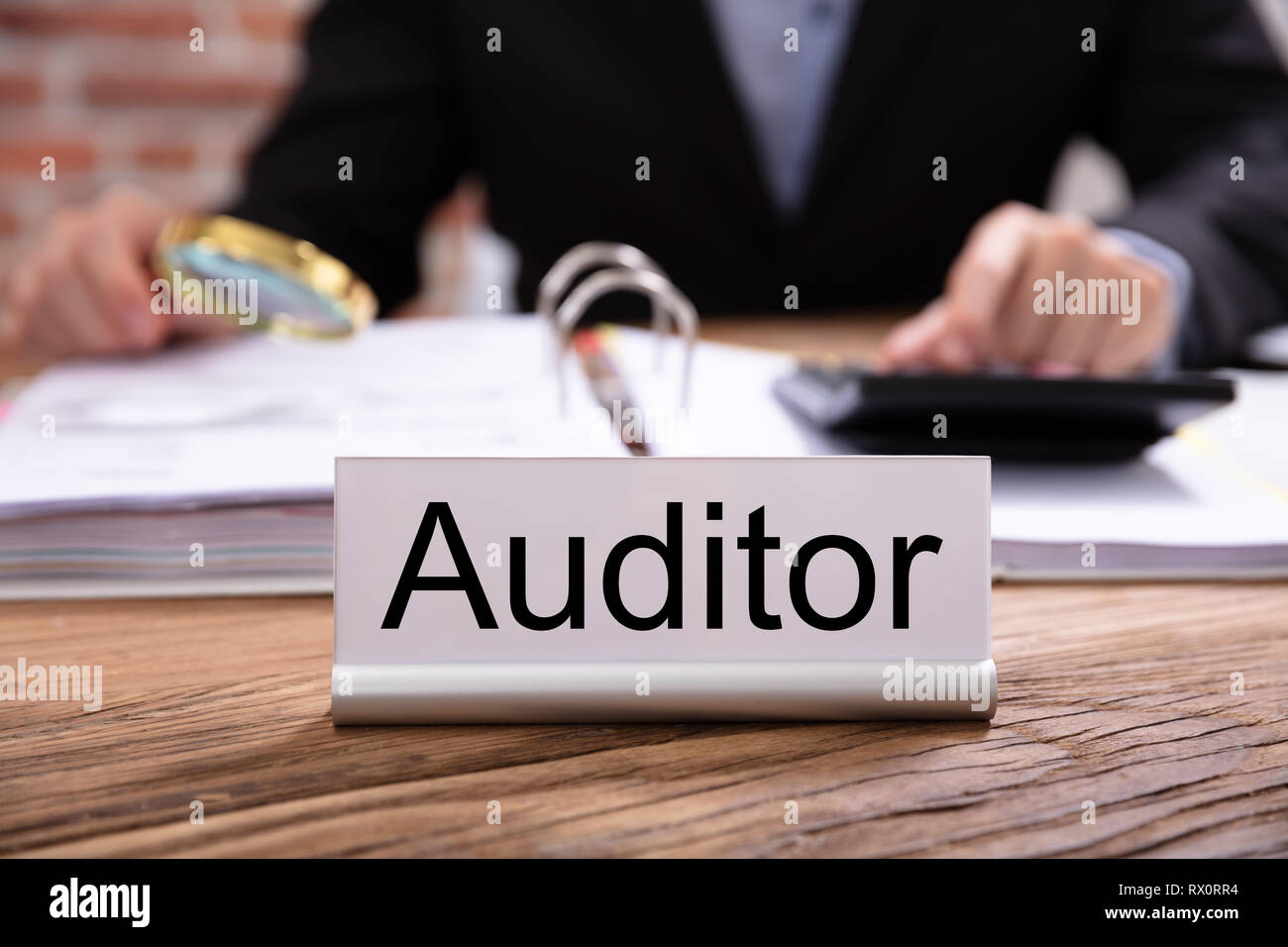 Nameplate With Auditor Title Kept On Desk In Front Of Businessman Examining The Invoices Stock Photo