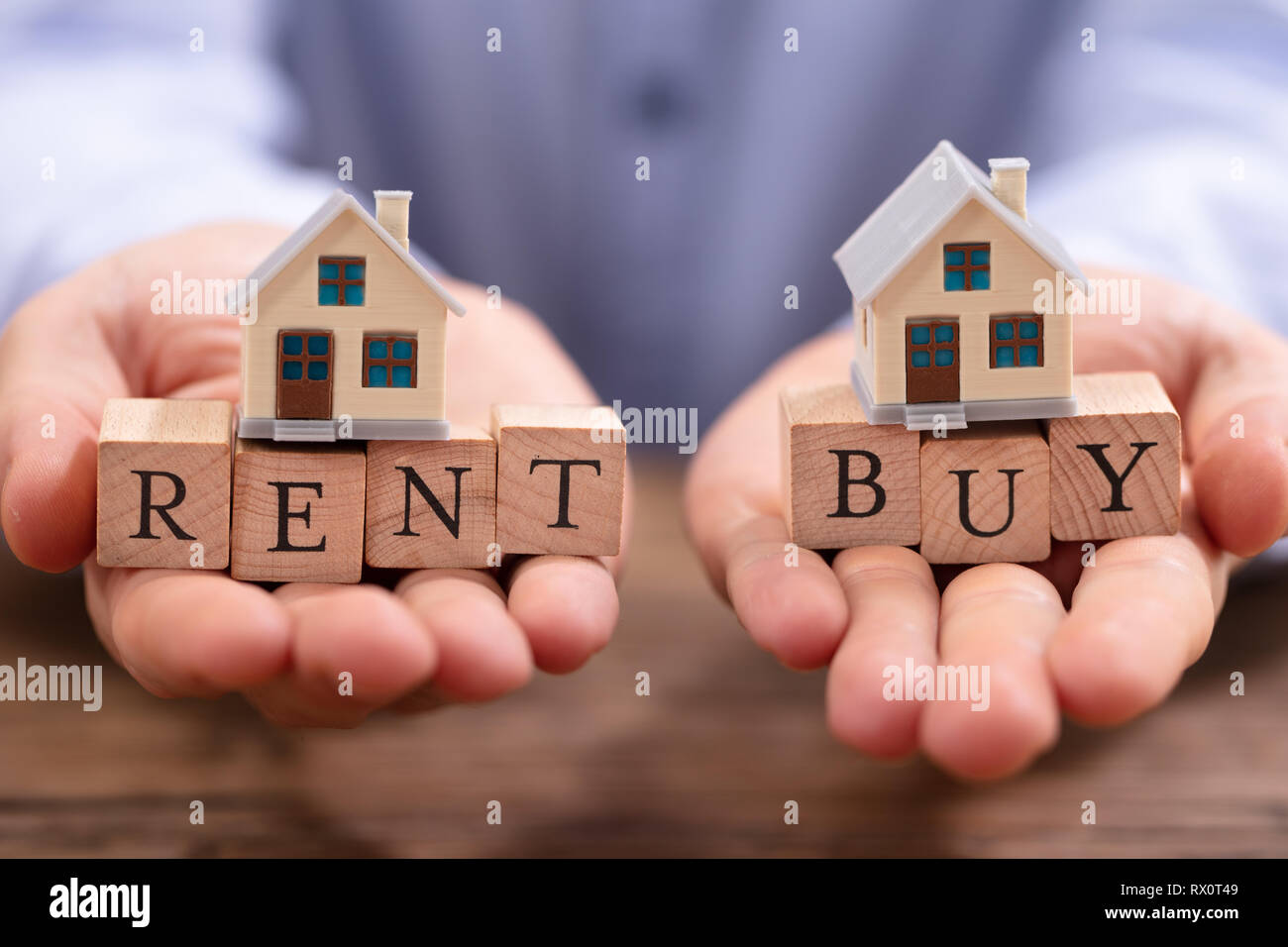 Close-up Of A Businessman's Hand Balancing Rent And Buy Blocks With House Model Stock Photo