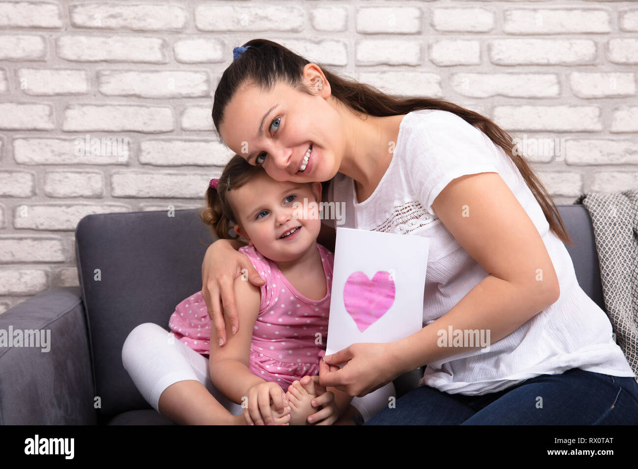 Smiling Mother Hugging Her Little Daughter Holding Love Card In Hand At Home Stock Photo