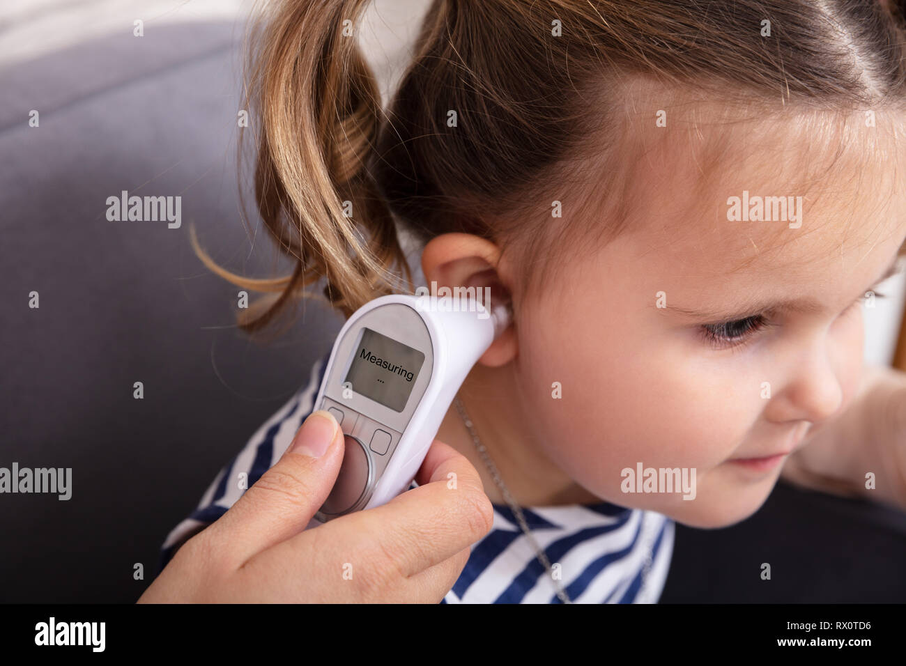 Close-up Of Hand Checking Girl's Ear With Digital Thermometer Stock Photo