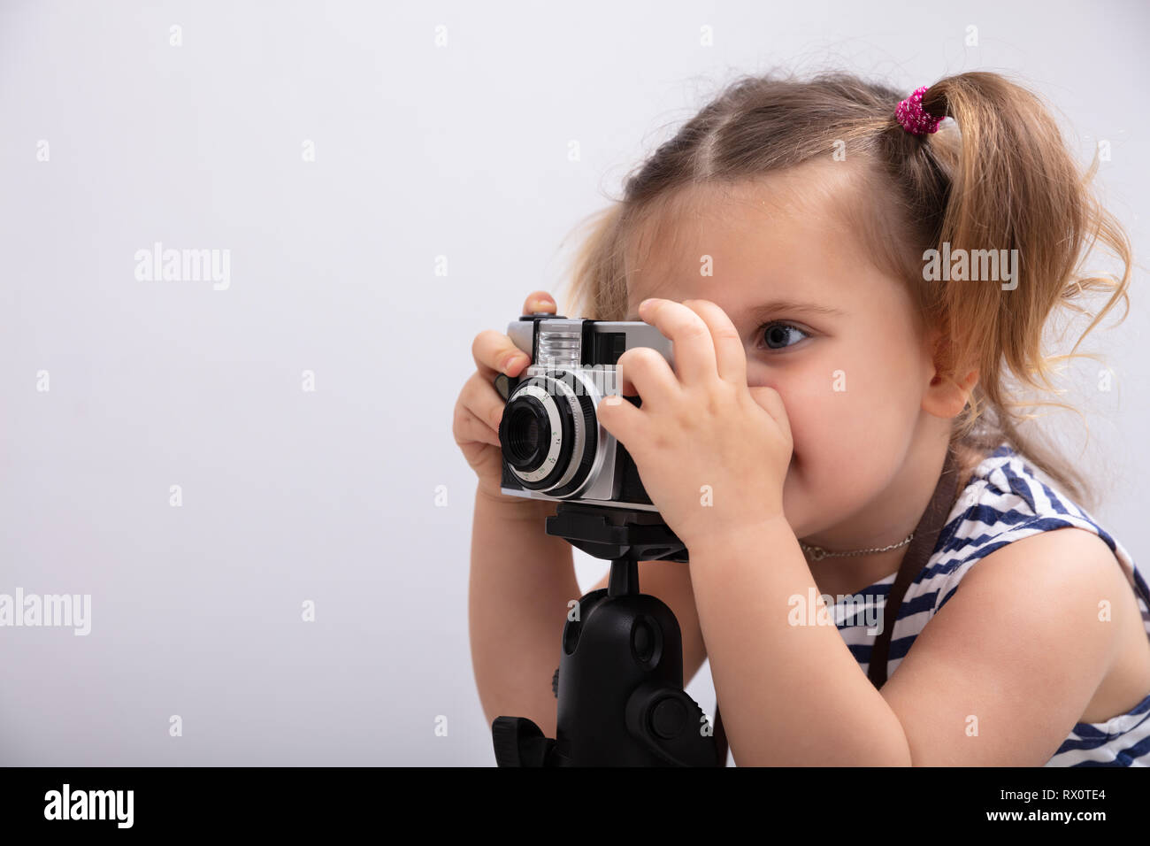 Little Girl Standing Against White Background While Taking Picture Using Photo Camera Stock Photo