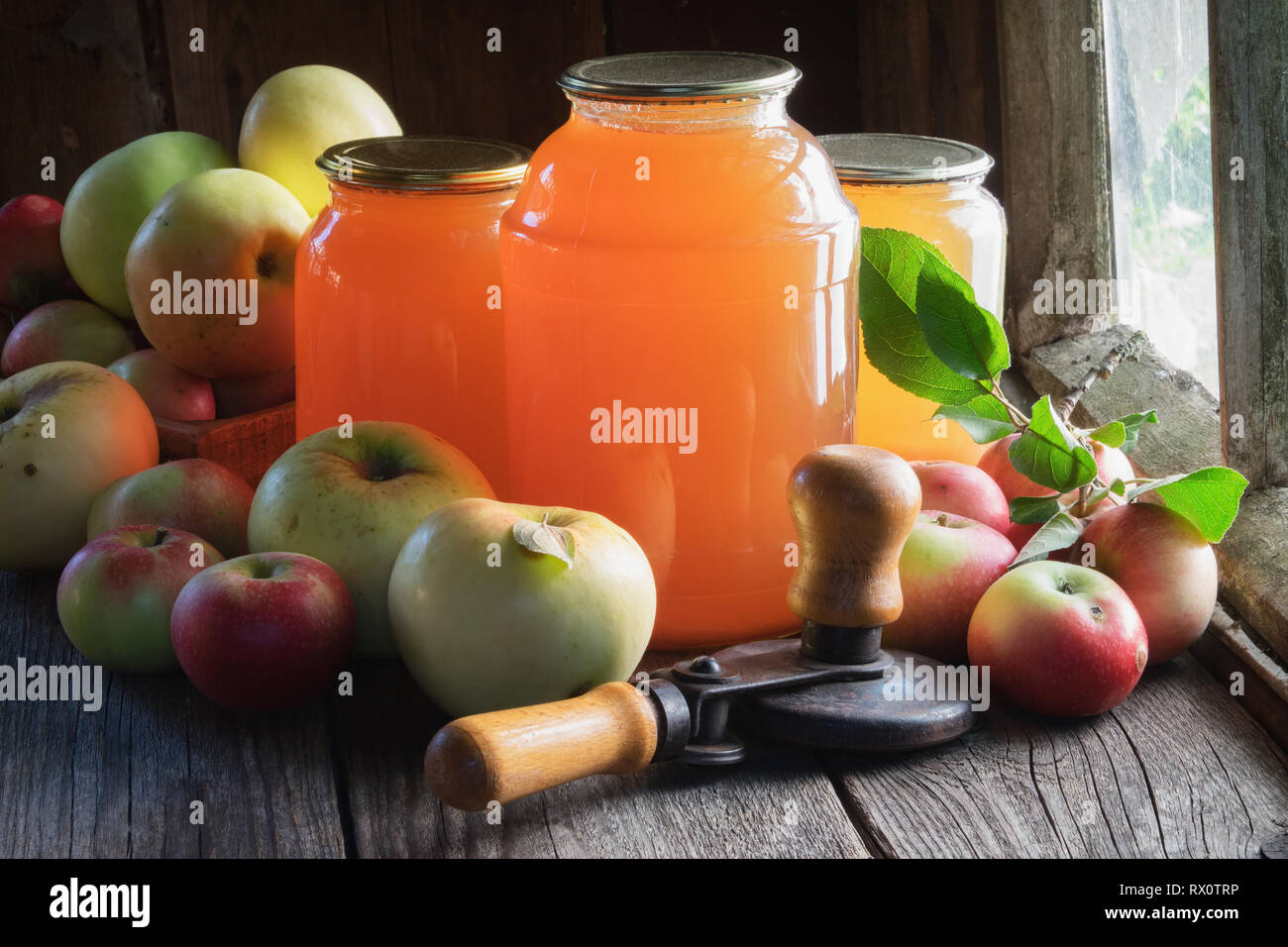 Glass jars of apple juice, apple fruits and can lid closing machine for canning. Stock Photo