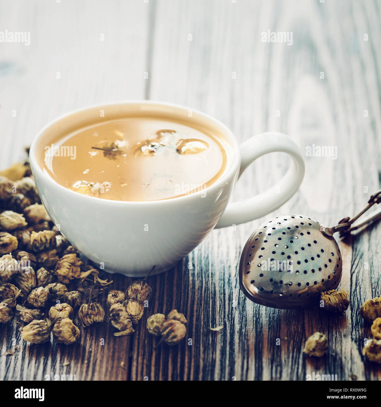 Healthy chamomile tea cup, strainer and dry daisy flowers. Stock Photo