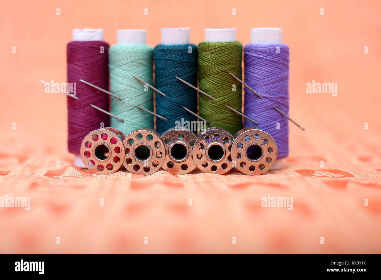 Portrait of multicolored sewing thread, needle and bobbin on the orange cloth. Stock Photo