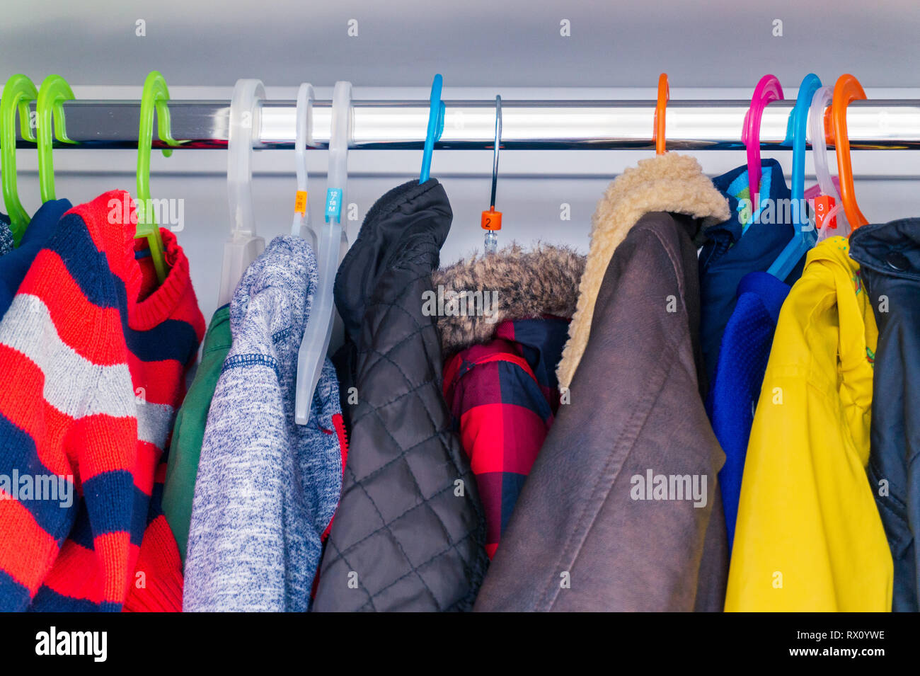 Little boy's child size jackets, coats and sweaters hanging in a kid's closet with colorful hangers. Preparing for winter with warm clothing for kids. Stock Photo