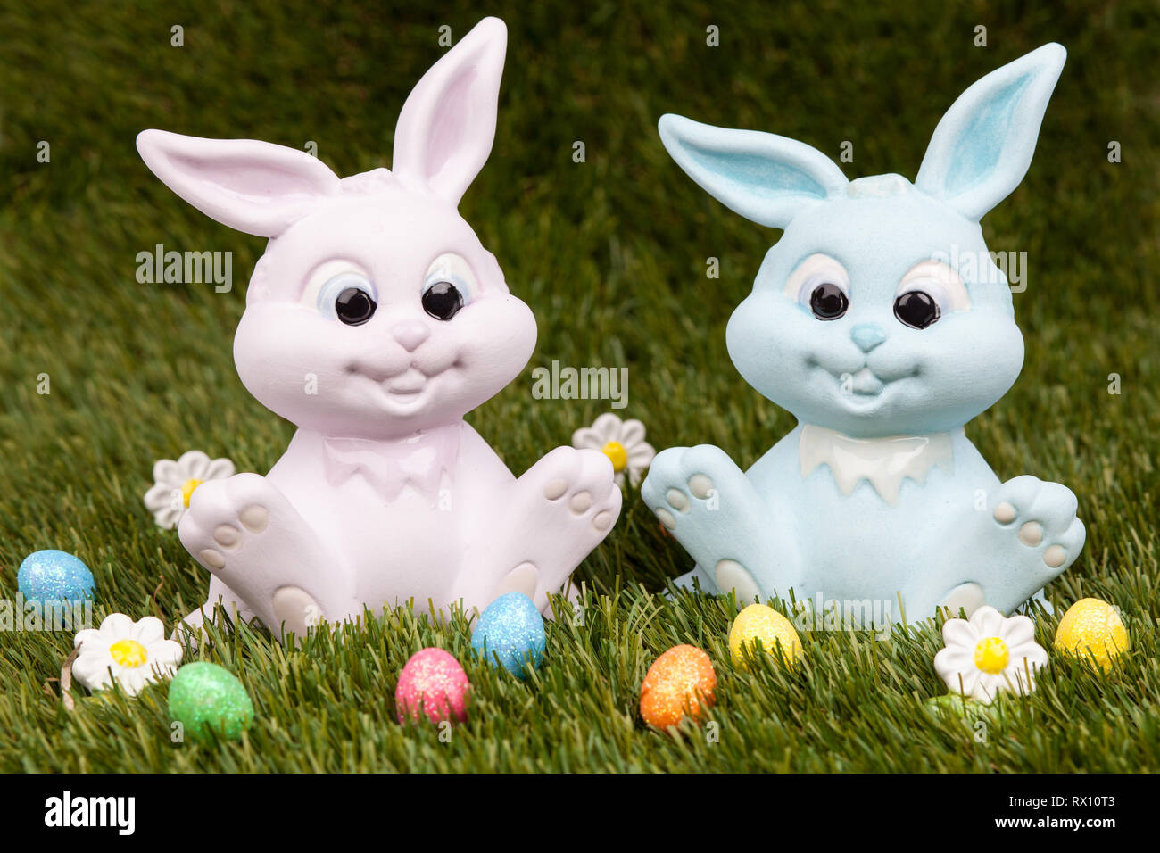 Easter bunnies sitting on grass surrounded by colourful easter eggs Stock Photo