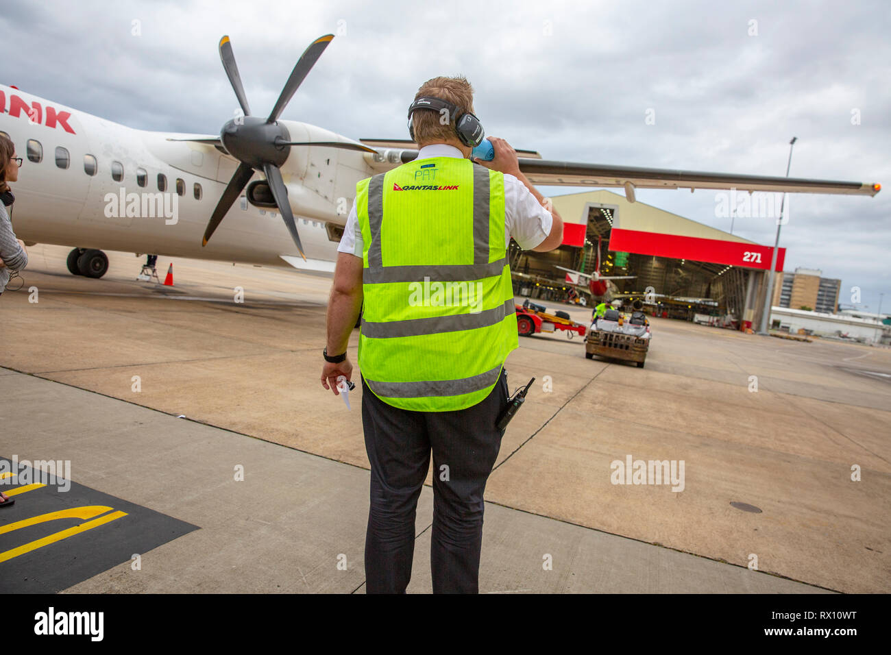 Qantas Link employee in high viz vest airside at Sydney airport awaits luggage to be unloaded from an inbound Qantas flight plane,Sydney,Australia Stock Photo