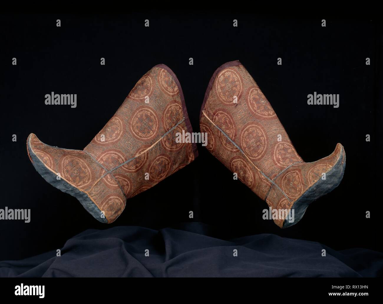 Pair of Woman's Boots with Tying Ribbon. China. Date: 900 AD-1000. Dimensions: a: 40 × 29.2 cm (15 3/4 × 11 1/2 in.)  b: 39.2 × 28.6 cm (15 3/8 × 11 1/4 in.)  Repeat: 13.2-14 × 12 cm (5 1/8-5 1/2 × 4 3/4 in.)  c (ribbon): 1.45 × 60.8 cm (5/8 × 24 in.). Outer boot: silk, complementary weft twill weave with inner warps; seam trim cord: silk, oblique interlacing; ribbon and top boot edge binding: silk, simple and complex gauze weave; lined with silk, plain weave; lining's upper edge facing: silk, twill damask weave; sole: silk, plain weave; tying ribbon: twill weave self-patterned by areas of twi Stock Photo