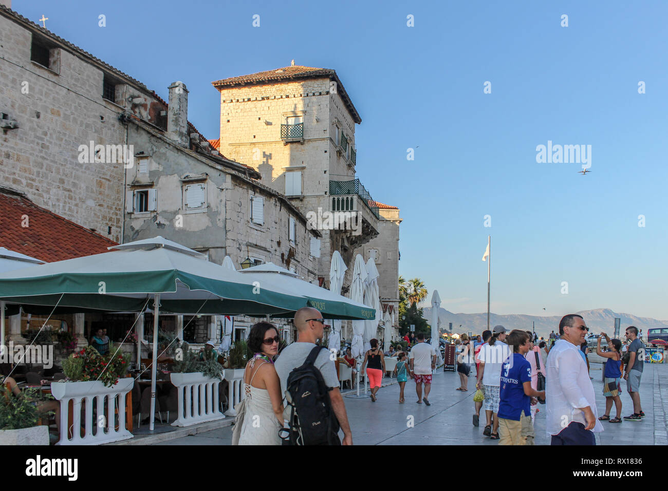 Trogir promenade & Mala Loza (loggia/gallery) busy with tourists.  A plane is taking off from split airport in the background Stock Photo
