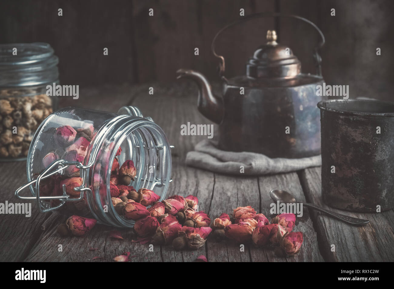 Vintage teapot, cup of healthy herbal tea, glass jars of dry rose buds