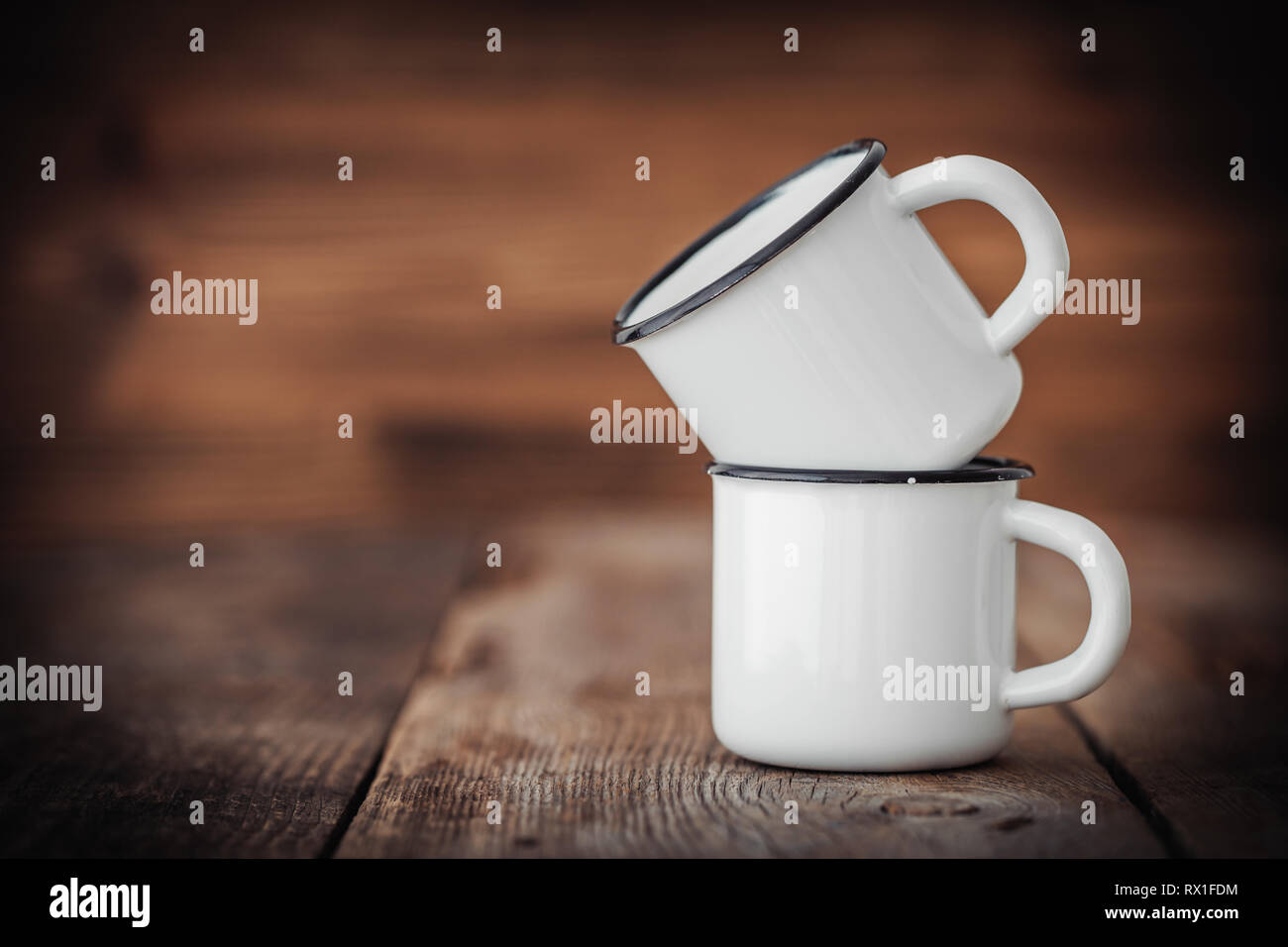 Two enameled cups on wooden rustic kitchen table. Stock Photo
