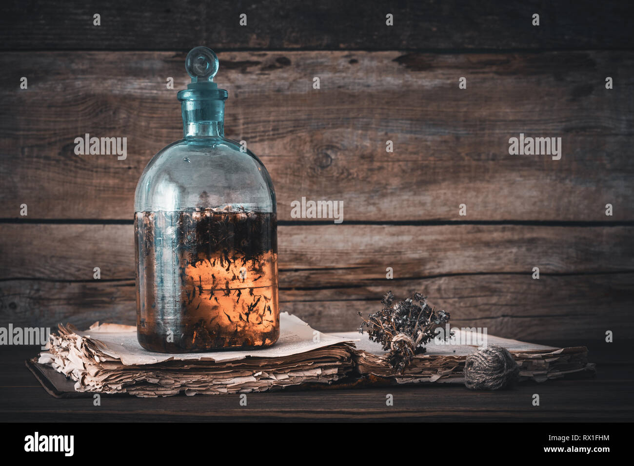 Tincture or potion bottle, old book and bunch of dry healthy herbs. Herbal medicine. Retro styled. Stock Photo