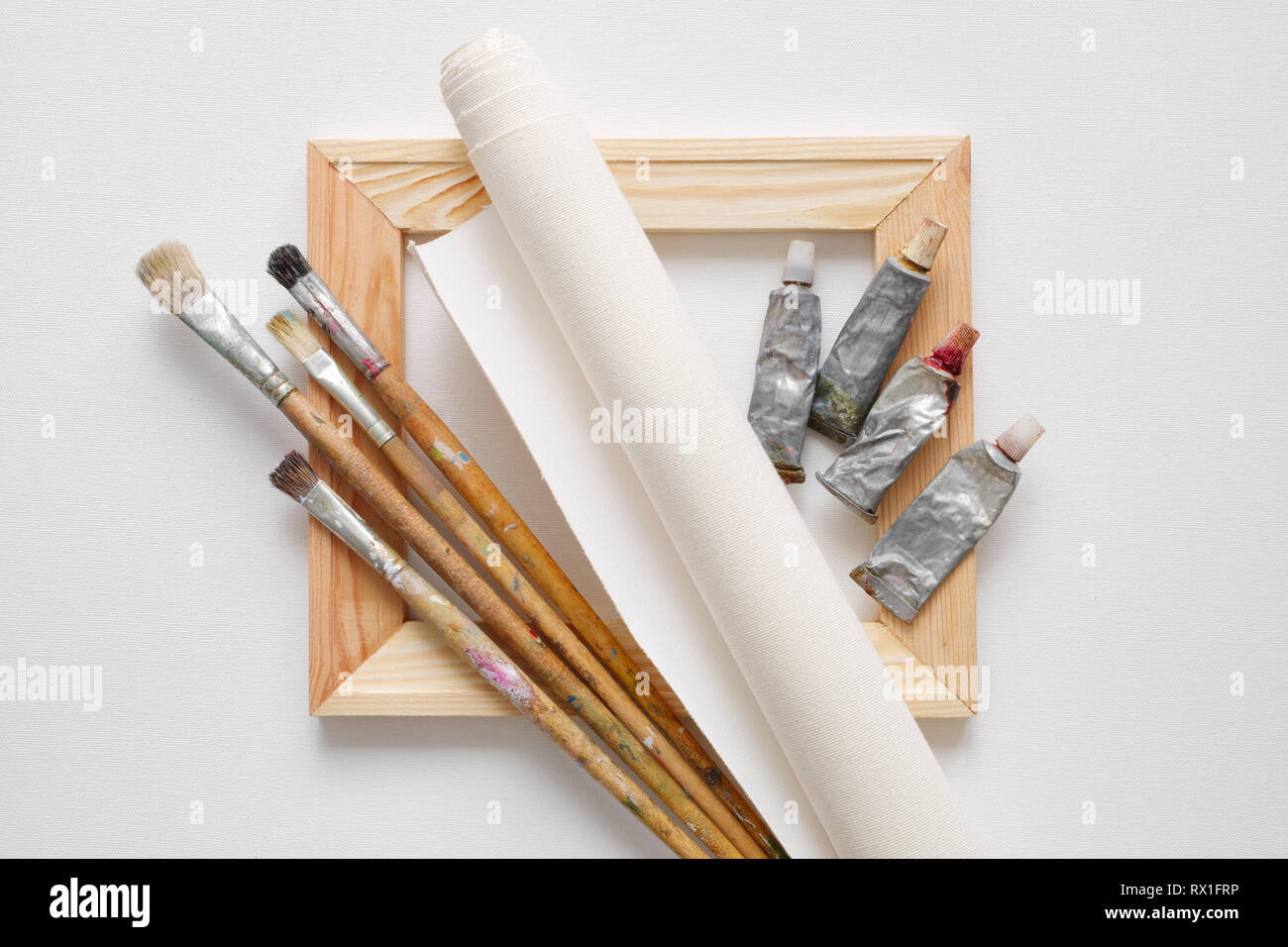 Wooden stretcher bar, paintbrushes, roll of artist canvas and paint tubes on white canvas background. Top view. Stock Photo