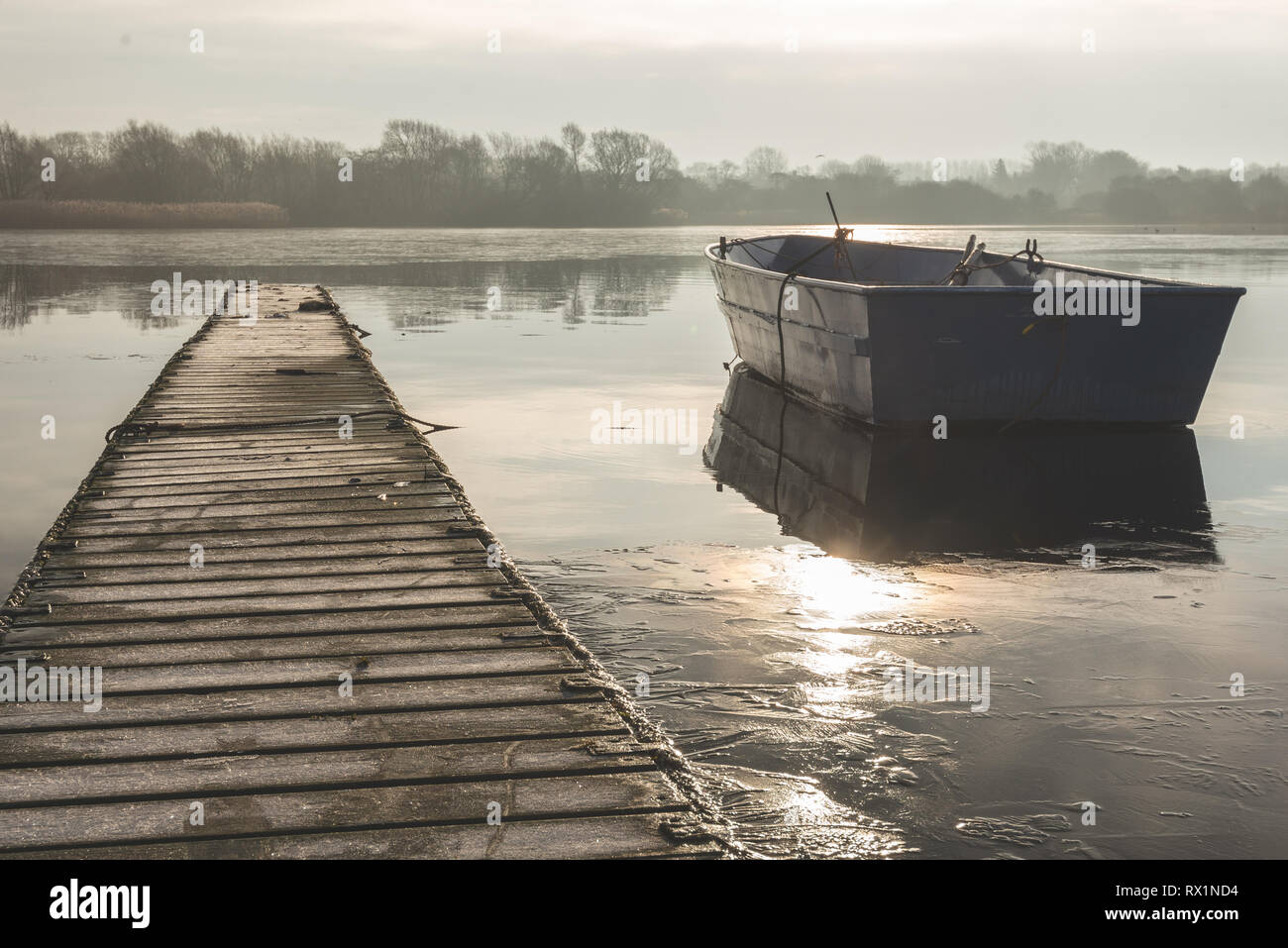 A rowing boat floats adrift on a frozen lake beside an empty walkway at