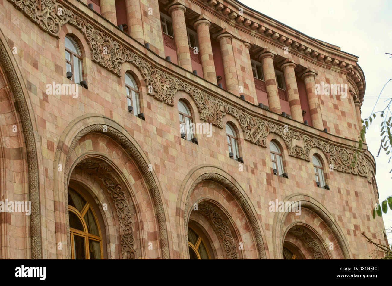 The upper corner of the administrative building on the square in Yerevan built of colorful stone, with loggias, columns, arches and beautiful edging o Stock Photo